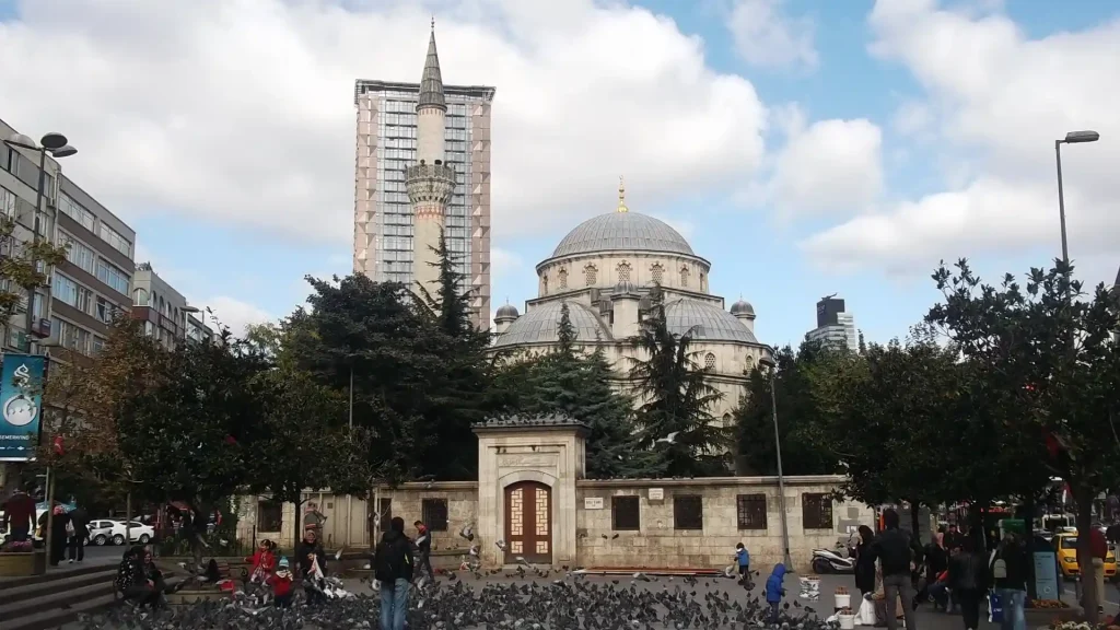 Şişli'de bir grup insanın etrafında toplanmış kuşlar ve bir cami yapısı.